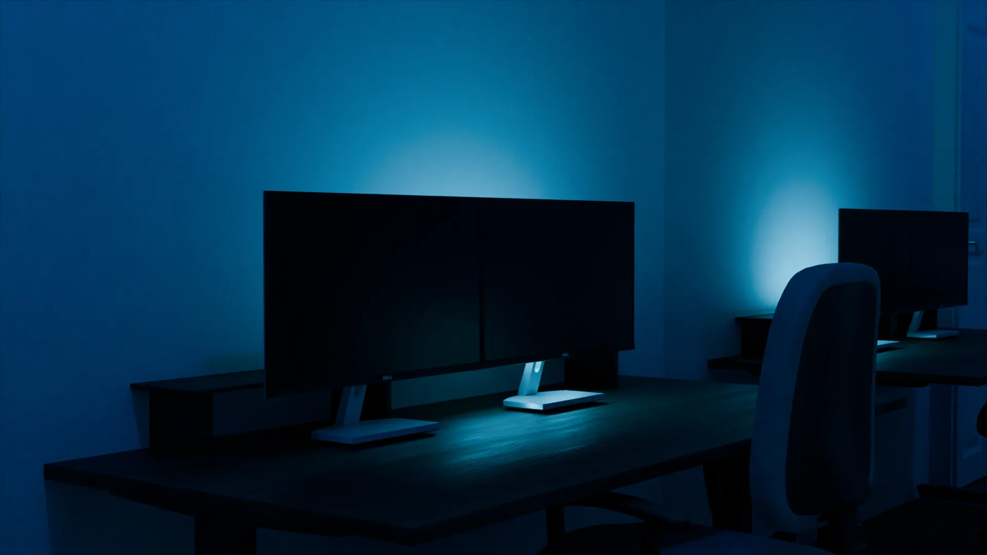 Le bureau : deux écrans, chaise, rétroéclairage bleu contre le mur.