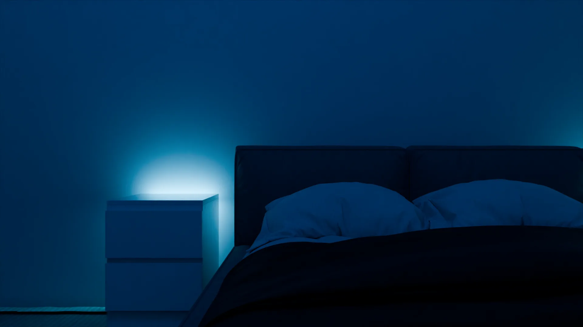 Le lit et la table de chevet, éclairés par une lumière bleue diffuse.
